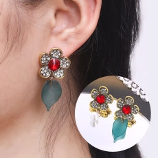 Close-up of vintage flower earrings with red gemstone and matte green leaf charms