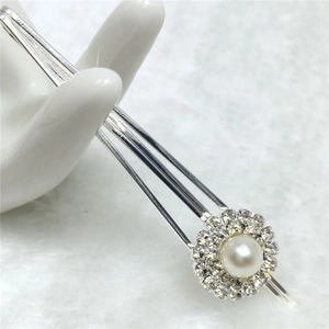 Détail d'une pince à cheveux argentée avec fleur de perle et strass sur main en céramique