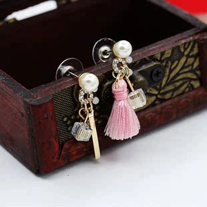 Detail of asymmetric pearl earrings with pink tassels and a clear cube on a wooden box
