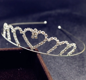 Detail view of a silver rhinestone tiara with heart patterns on a brown velvet box