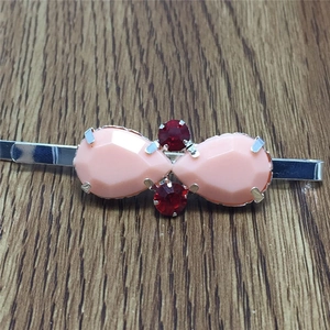 Détail d'une barrette argentée ornée de gemmes roses en goutte et rouges rondes facettées