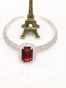 Gros plan d'un collier ras de cou argenté avec grand cristal rouge et trois rangées de strass