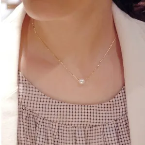Détail d'un collier en chaîne dorée élégante avec une perle blanche sur le cou