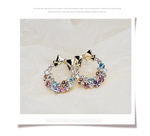 Detail of colorful crystal wreath earrings with golden bow on elegant lace background