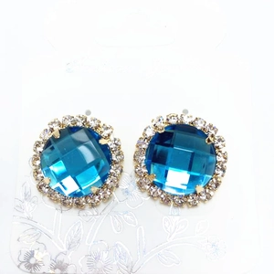 Detail view of round blue gemstone stud earrings with white crystal halo and gold base