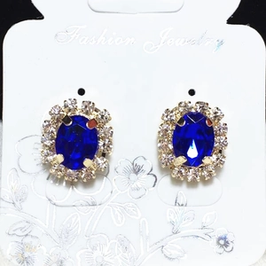 Detail of flower stud earrings with dark blue oval gemstone and white crystal halo
