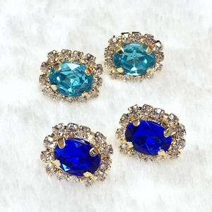 Detailed macro view of oval crystal stud earrings with a clear rhinestone halo in two shades of blue