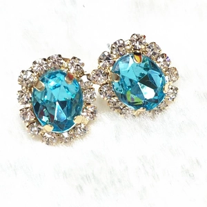 Close-up of blue oval gemstone earrings with clear crystal halo and gold plating