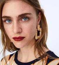 Close-up of model wearing large golden hoop earrings with unique hammered metal texture