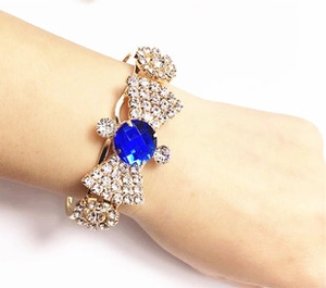 Detail of a gold-tone open bangle featuring blue center stone and pave rhinestones