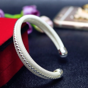 Detailed macro view of silver mesh textured open cuff bracelet on red velvet background