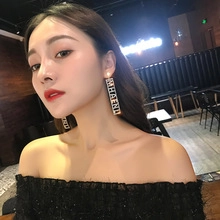 Close-up of sparkling rhinestone rectangle drop earrings with letter design on model