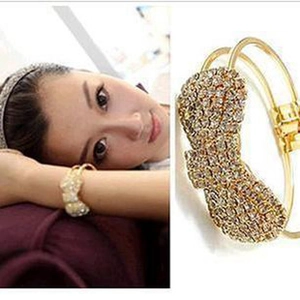 Macro detail of a gold-tone bangle with a large sparkling rhinestone bow for women