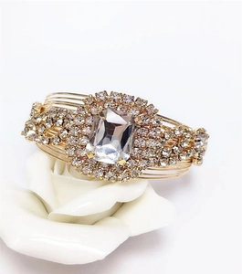Close-up of gold wide bangle with rectangular crystal and micro rhinestones on white rose