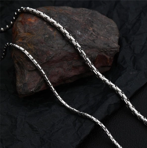 Polished silver stainless steel square chain necklace displayed on a dark textured rock