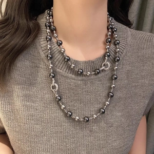 Détail d'un collier de perles grises à deux rangs porté sur un pull en maille marron