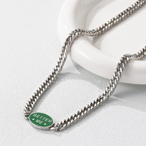 Close-up of silver Cuban chain with green enamel Better Me pendant on white surface