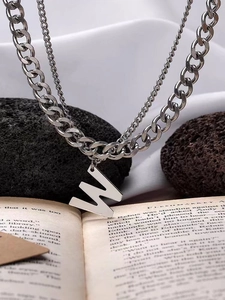 Detail of a layered silver necklace with a W pendant on a curb chain and thin chain