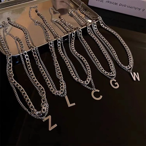 Detailed macro view of silver double-layered necklaces featuring letter pendants Z, L, C, G, W