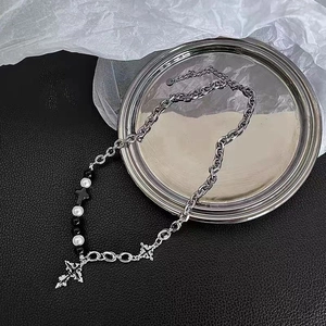 Macro shot of silver cross pendant with black and pearl beads on gothic cuban chain