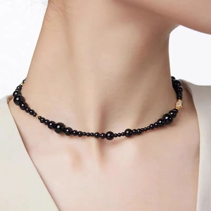 Détail macro d'un collier de perles noires avec pendentif carré doré sur le cou