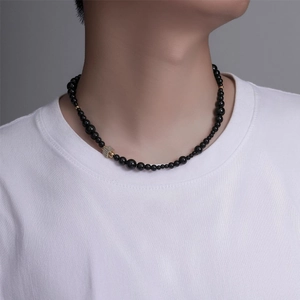 Détail d'un collier de perles noires avec un pendentif carré brillant sur un t-shirt blanc