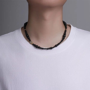 Gros plan d'un collier de perles noires avec pendentif carré doré sur un t-shirt blanc