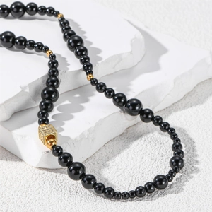 Détail d'un collier de perles noires avec pendentif carré doré sur pierre blanche