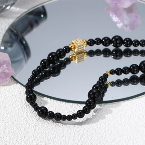 Collier de perles noires avec pendentif carré doré en zircone et reflet sur miroir