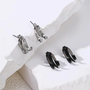 Minimalist silver and black claw-shaped drop stud earrings on white stone display