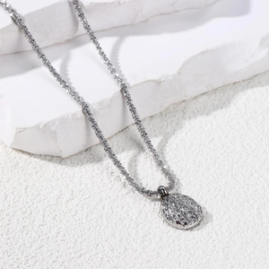 Macro shot of silver-toned necklace with textured chain and embossed oval pendant
