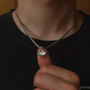 Detailed close-up of a golden cross necklace with mother of pearl inlay on flat snake chain
