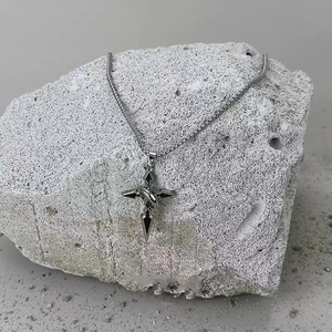 Gros plan détaillé d'un pendentif croix gothique en acier titane sur une pierre grise
