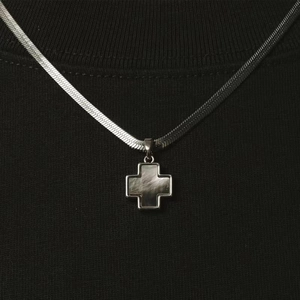 Macro shot of silver titanium steel cross pendant with dark shell inlay on black fabric