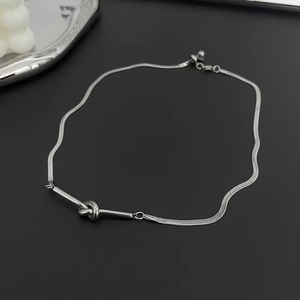 Detail of silver knot pendant necklace on a sleek black background with a white candle decor