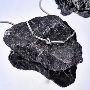 Minimalist silver knot pendant necklace with snake chain displayed on black mineral stone