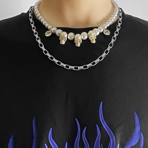Close-up of layered pearl necklace with gold skull pendants and silver block chain