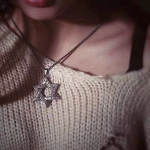 Close-up of a vintage stainless steel hexagram pendant worn over a beige sweater