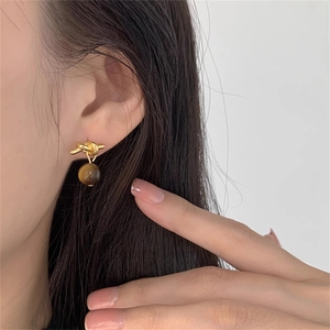 Detailed close-up of gold knot earrings with brown tiger eye stone on model ear