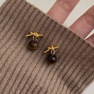 Close-up of golden knot earrings with cylinder tiger eye stones on brown knit sweater