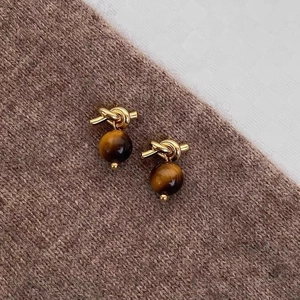 Detail of tiger eye stone stud earrings with golden knot and glossy gemstone finish