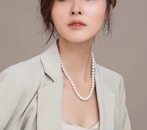 Elegant woman wearing a white pearl necklace and matching stud earrings with a beige suit
