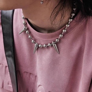 Punk style beaded chain necklace with silver cone spikes worn on a pink sweater