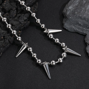 Macro shot of silver ball chain with industrial punk spike pendants on dark stone background