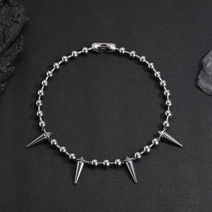 Close-up of silver punk ball chain necklace with pointed cone spike pendants on black rock