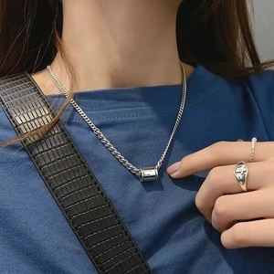 Vue détaillée du pendentif cylindrique en acier argenté et de la chaîne plate