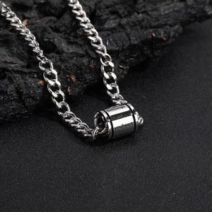Détail d'un pendentif cylindre argenté avec gravure sur une chaîne à mailles cubaines