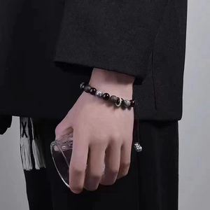 Close-up of snowflake obsidian and lava stone braided bracelet worn by a model in a suit
