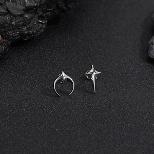 Macro shot of polished silver star and crescent moon stud earrings on dark background