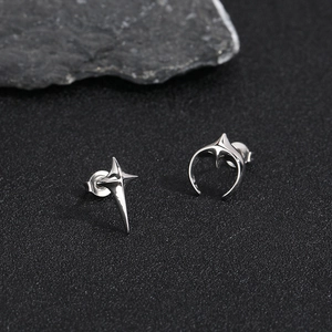 Modern silver star and crescent moon stud earrings on dark stone background